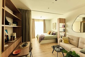 Una sala moderna con sofá, mesa de centro, comedor con mesa y sillas, y un dormitorio con cama y cortinas.