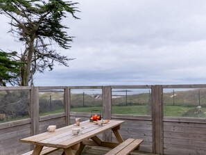 A wooden deck with a picnic table and benches, overlooking a grassy landscape and a body of water. - Magnificent Beach House for 6 (Ploudalmezeau)