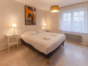 Ein Schlafzimmer mit einem Bett, zwei Nachttischen, einer Lampe, einer Heizung und einem Fenster mit Vorhängen.