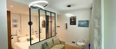 Une chambre à coucher moderne avec un lit, un canapé, un miroir et un tableau accroché au mur.