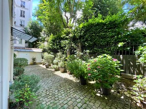 Ein Innenhof mit Kopfsteinpflasterweg, Kübelpflanzen und einem Metallzaun.