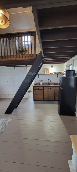 Una cocina con armarios de madera, un refrigerador negro y una escalera con barandilla de metal.