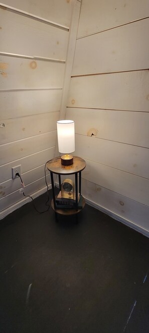 Ein kleiner Tisch mit Lampe, einer Uhr, einer Steckdose und einer Wand mit horizontalen Holzpaneelen.