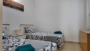 A bedroom with two beds, a nightstand, a lamp, a dresser, and a painting on the wall. - Apartment in El Verger, 800 metres from the sea, with garden and communal pool (El vergel)