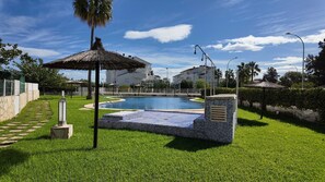 Une piscine avec une terrasse carrelée, un palmier et un gazebo à toit de chaume.