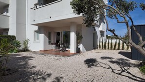 A modern two-story building with a covered patio area, a gravel driveway, and a small garden with various plants. - Apartment in El Verger, 800 metres from the sea, with garden and communal pool (El vergel)