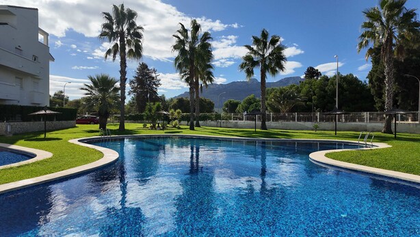 A swimming pool with palm trees, a grassy area, and a mountain in the background. - Apartment in El Verger, 800 metres from the sea, with garden and communal pool (El vergel)