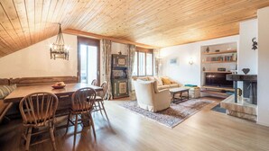 Un salon chaleureux avec un plafond en bois, un coin repas avec une table et des chaises, un canapé et une cheminée.