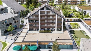 Un immeuble à plusieurs étages, doté d’un toit plat, d’un espace extérieur couvert aménagé en coin salon et d’une enseigne indiquant « Sport et mode ».
