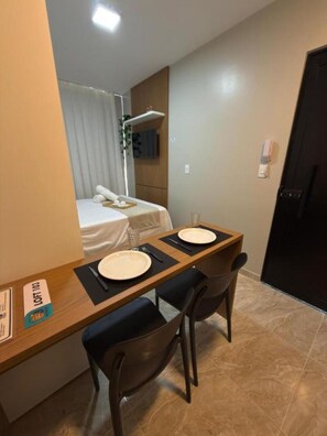 A compact room with a bed, a small table with two plates, and two chairs.