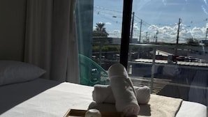 A hotel room with a bed, a tray with two cups, and a view of the city through large windows.