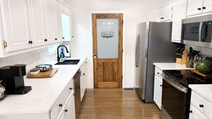 Une cuisine avec des armoires blanches, un réfrigérateur en acier inoxydable, un four à micro-ondes et une porte en bois portant l’inscription « GARDEMANGER ».