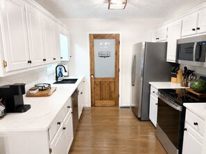 A kitchen with white cabinets, a stainless steel refrigerator, a microwave, and a wooden door labeled 'PANTRY'. - Stunning lakefront views for a perfect sunset! (Eatonton)