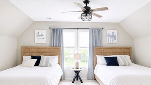 Une chambre avec deux lits, un ventilateur de plafond, une petite table avec une lampe et des œuvres d’art accrochées aux murs.
