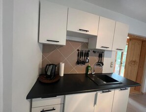 A kitchen with white cabinets, a black countertop, and a stainless steel sink. - Holiday Home With Private Garden, Close to the sea (Rewal)
