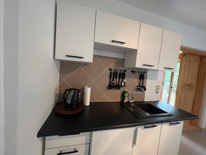 A kitchen with white cabinets, a black countertop, and a stainless steel sink. - Holiday Home With Private Garden, Close to the sea (Rewal)