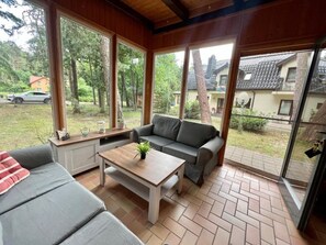 A room with a sofa, a coffee table, and a window overlooking a garden and buildings. - Holiday Home With Private Garden, Close to the sea (Rewal)