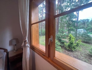 Ein Zimmer mit großem Fenster, einem Nachttisch mit Lampe und einem Vorhang.