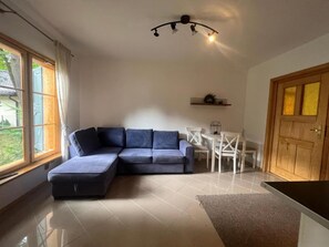 A modern living room with a sectional sofa, a dining table with chairs, a kitchen area, and a large window. - Holiday Home With Private Garden, Close to the sea (Rewal)