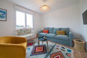 A living room with a sofa, a yellow chair, a round coffee table, a patterned rug, and a hanging light fixture. - Holiday Retreat in Landeda Near Sandy Beaches (Landeda)