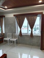Una habitación con dos sillas blancas, una mesa de madera y una ventana con cortinas.
