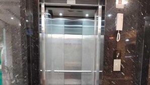 Un ascensor moderno con puerta de cristal, un felpudo rojo en la entrada y una pared de mármol.