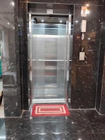 Un ascensor moderno con puerta de cristal, un felpudo rojo en la entrada y una pared de mármol.