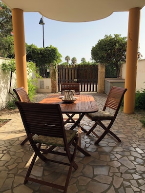 A covered outdoor patio with a stone floor, wooden chairs, a table, and a decorative item in the center. - Townhouse just a stone's throw from the sea (Porto Cesareo)