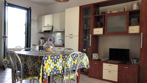 A dining area with a table set for four, a television on a wooden cabinet, and a kitchen in the background. - Townhouse just a stone's throw from the sea (Porto Cesareo)