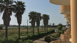 A view of a building with a curved balcony, palm trees, and a pathway. - Townhouse just a stone's throw from the sea (Porto Cesareo)