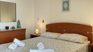 A bedroom with a wooden bed, a nightstand with a lamp, a dresser, a mirror, and a wall-mounted picture. - Townhouse just a stone's throw from the sea (Porto Cesareo)