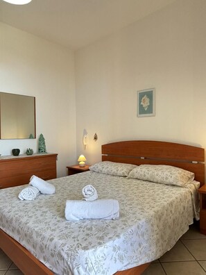 A bedroom with a wooden bed, a nightstand with a lamp, a dresser, a mirror, and a wall-mounted picture. - Townhouse just a stone's throw from the sea (Porto Cesareo)