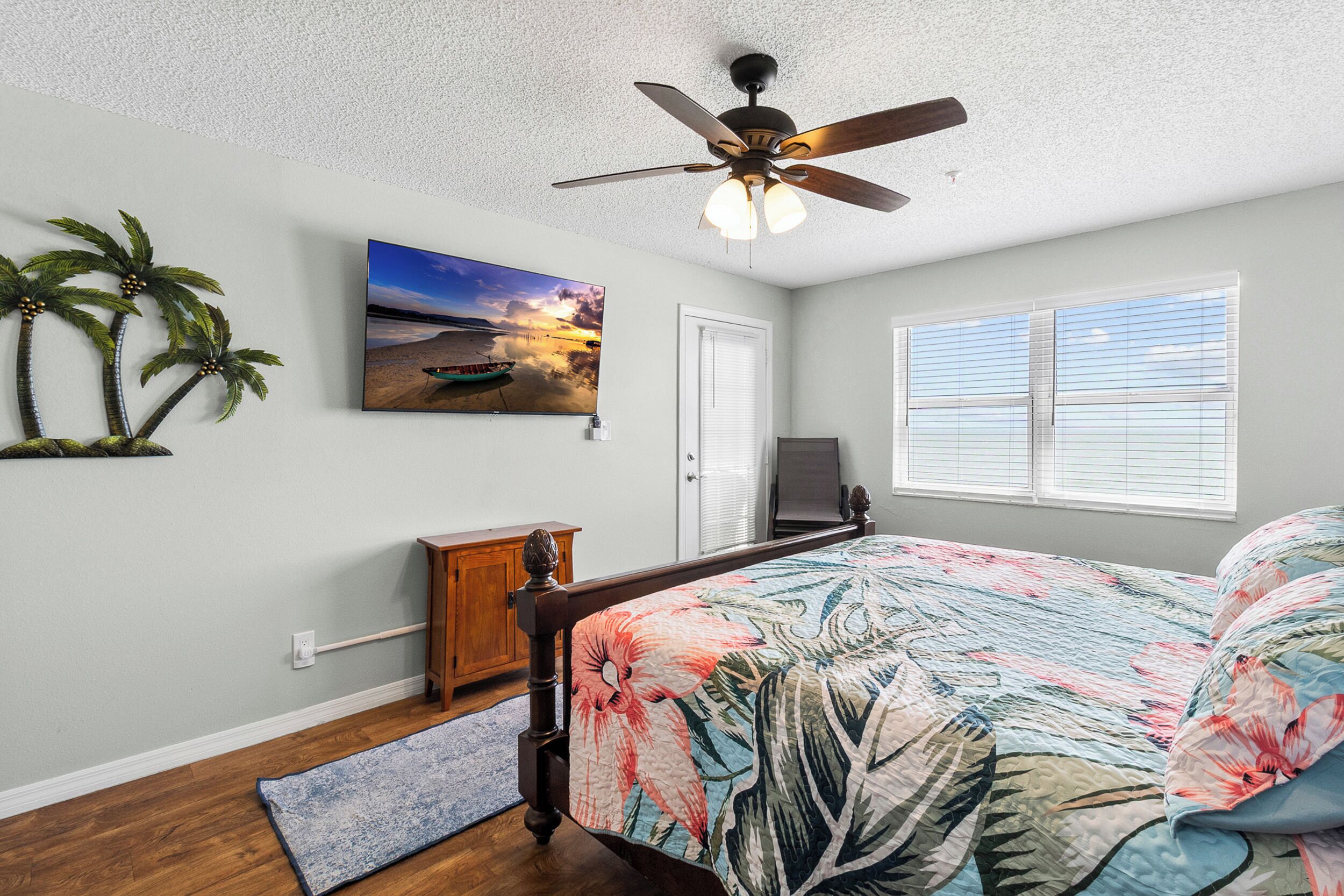 A bedroom with a bed, a ceiling fan, a painting, a wooden cabinet, and a window with blinds.