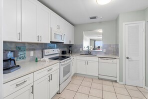 A modern kitchen with white cabinets, a microwave, stove, and a coffee maker. - Beach Front Near John's Pass - Sea Breeze #602 (Madeira Beach)