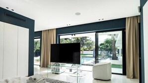 Quarto de hotel moderno com uma cama grande, uma televisão de tela plana, uma mesa de centro de vidro e vista para uma piscina.