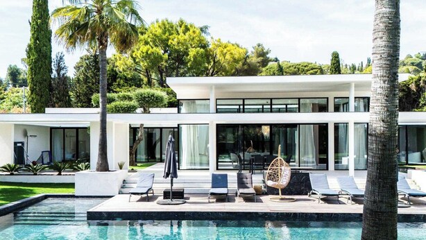 Uma casa moderna com piscina, espreguiçadeiras e um jardim tropical.