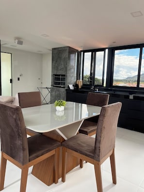 Een moderne eetruimte met een glazen tafel, houten stoelen en een keuken met een groot raam.