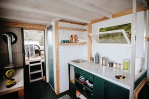 A compact kitchen with a built-in sink, wooden shelves, and a window overlooking greenery.
