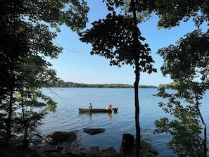 A calm lake with two people in a boat, surrounded by trees.