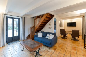 Ein Wohnzimmer mit einem blauen Sofa, einer Holztreppe, zwei Sesseln, einem Couchtisch und einem Fernseher.