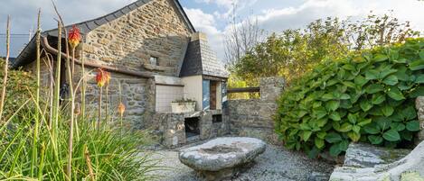 A stone building with a sloped roof, surrounded by gravel, plants, and a stone bench.