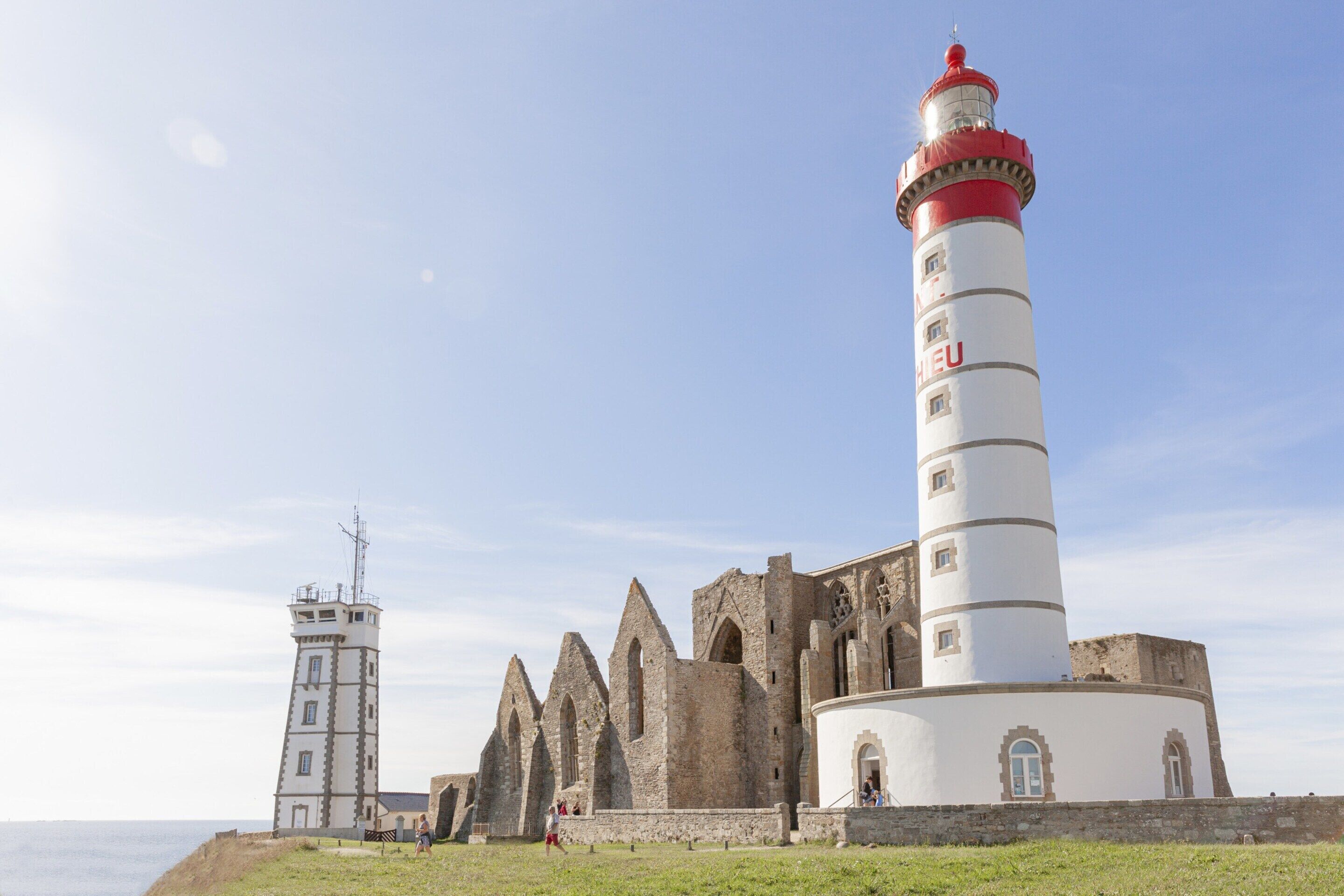 A historic lighthouse with a red top, adjacent to a medieval-style building with pointed arches and a circular tower.