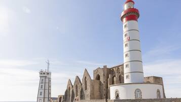 A historic lighthouse with a red top, adjacent to a medieval-style building with pointed arches and a circular tower.