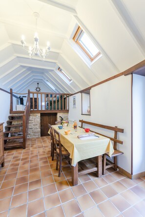 A dining area with a high ceiling, wooden staircase, and a chandelier. - Charming Breton House Near the Sea (Plouguerneau)