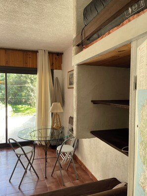 Ein Zimmer mit Glastisch und Stühlen, einer Lampe, einer Karte an der Wand und Blick auf Grünfläche.