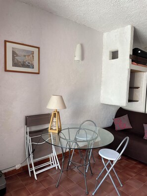 Ein Wohnzimmer mit Glastisch, Stühlen, einer Couch, einer Lampe und einem gerahmten Bild an der Wand.