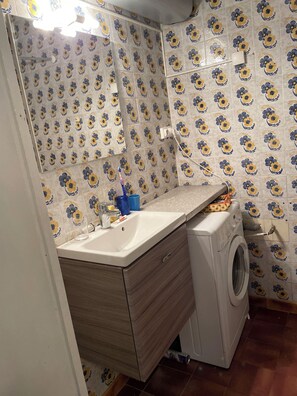 Ein Badezimmer mit gemusterten Fliesen, einem Waschbecken, einem Spiegel, einer Waschmaschine und einer Dusche.
