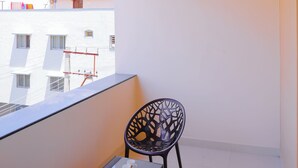 A balcony with a ceiling fan, two chairs, a small table, and a view of buildings. - Hotel Raaga Inn (Tirupati)