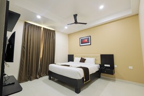 A hotel room with a bed, a flat-screen TV, a ceiling fan, and a painting on the wall. - Hotel Raaga Inn (Tirupati)