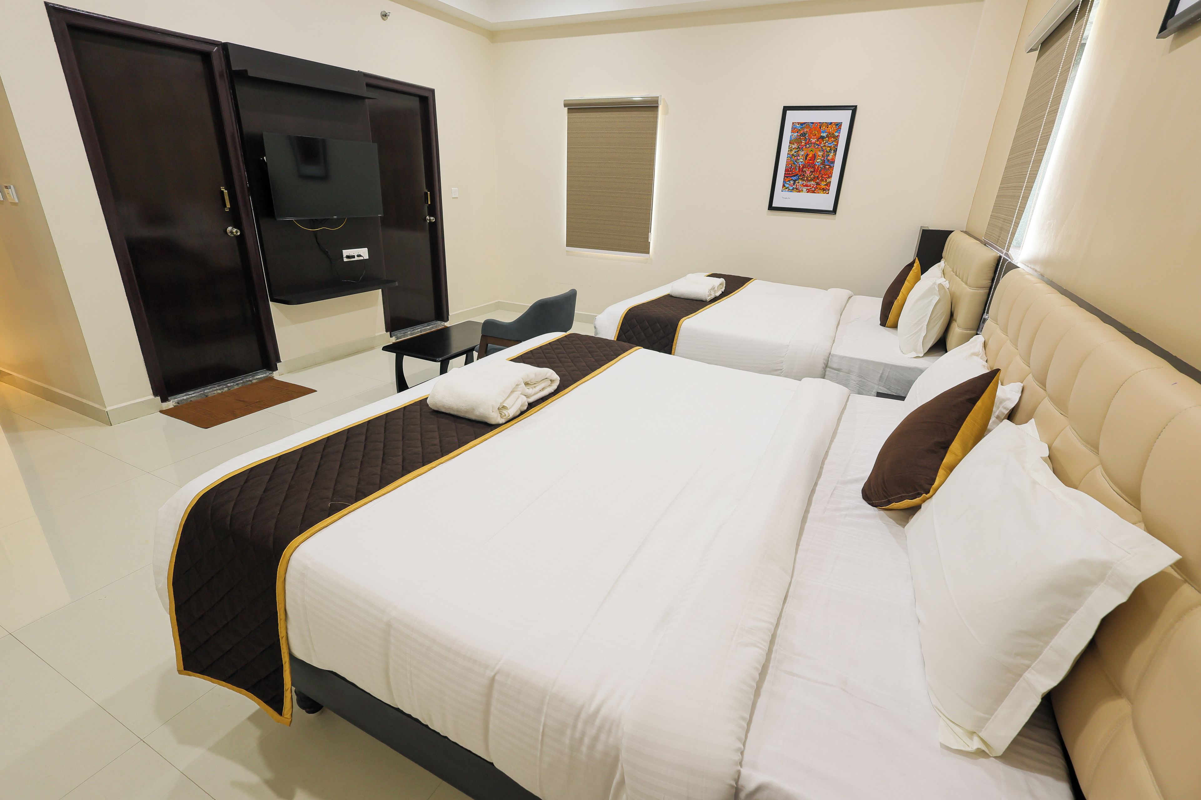 Habitación de hotel con dos camas, un escritorio, una silla, un armario y una ventana con persianas.
